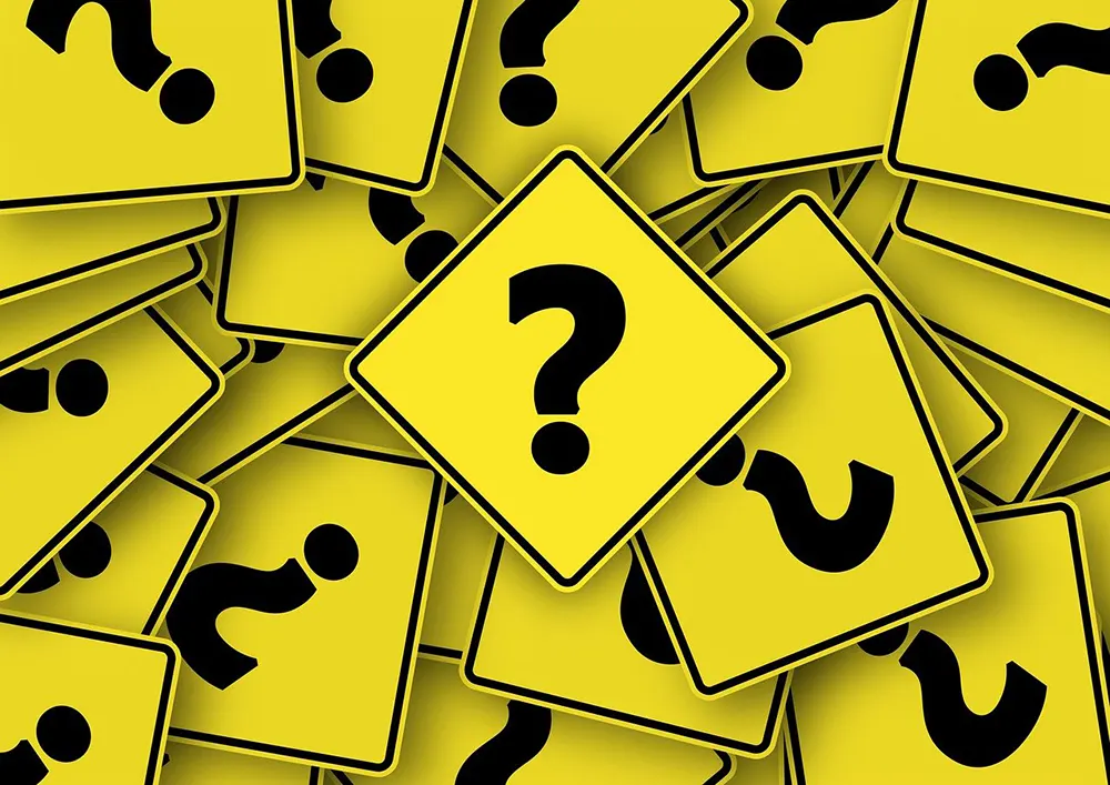 A pile of yellow road signs with black question marks, symbolizing confusion or uncertainty.