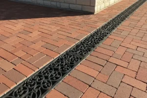 Benefits of French Drains - Decorative trench drain grate running through a brick paver driveway in front of a stone building.